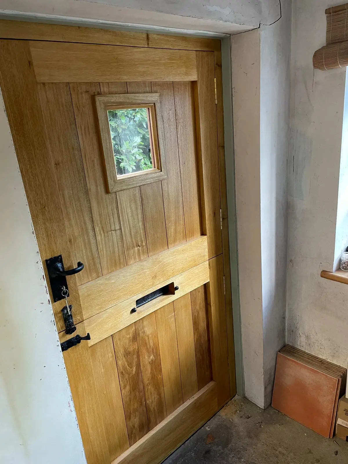 Fitted oak stable door with glazed light and thumb-latch, open to a garden beyond